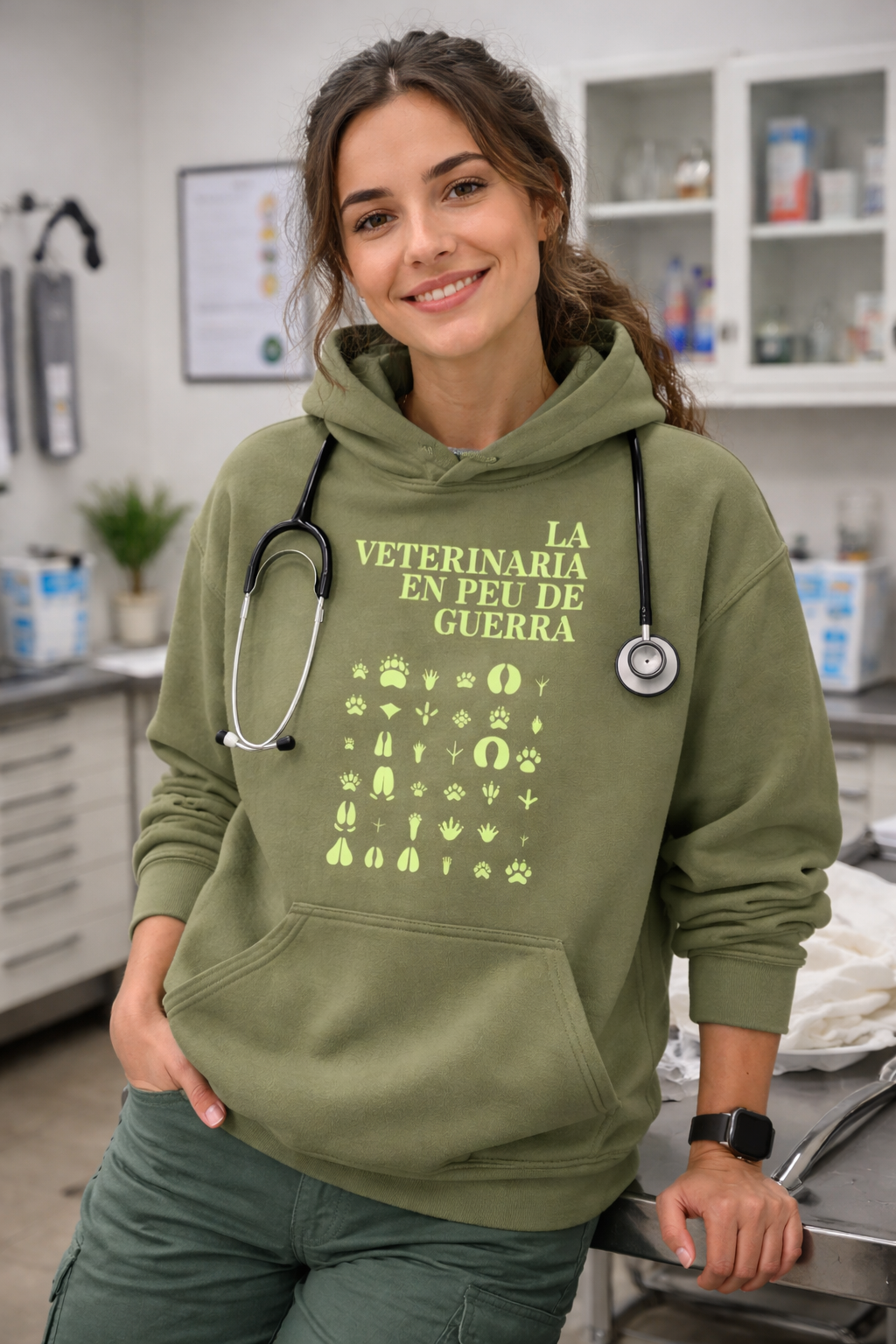 Sudadera veterinaria reivindicativa de color verde oliva con capucha para pet lovers comprometidos. La imagen muestra a una modelo sonriente en una clínica veterinaria con un estetoscopio y el mensaje 'LA VETERINARIA EN PEU DE GUERRA' con huellas de animales.