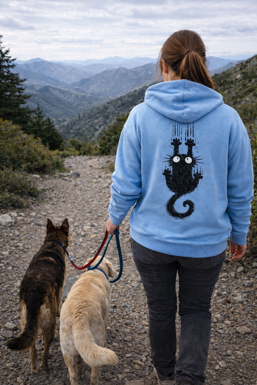 Persona paseando dos perros por un sendero de montaña vistiendo la sudadera azul con diseño de gato de Dogma BCN. Estilo de vida para pet lovers aventureros.